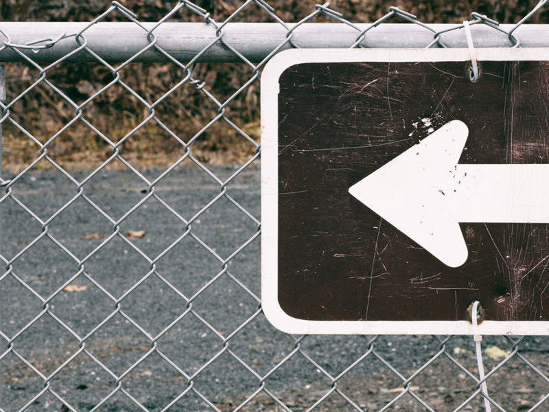 A sign on a fence displays a white arrow pointing to the left, indicating direction.