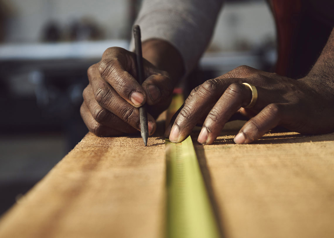 A person is engaged in woodworking, measuring a piece of wood with a ruler for precision.